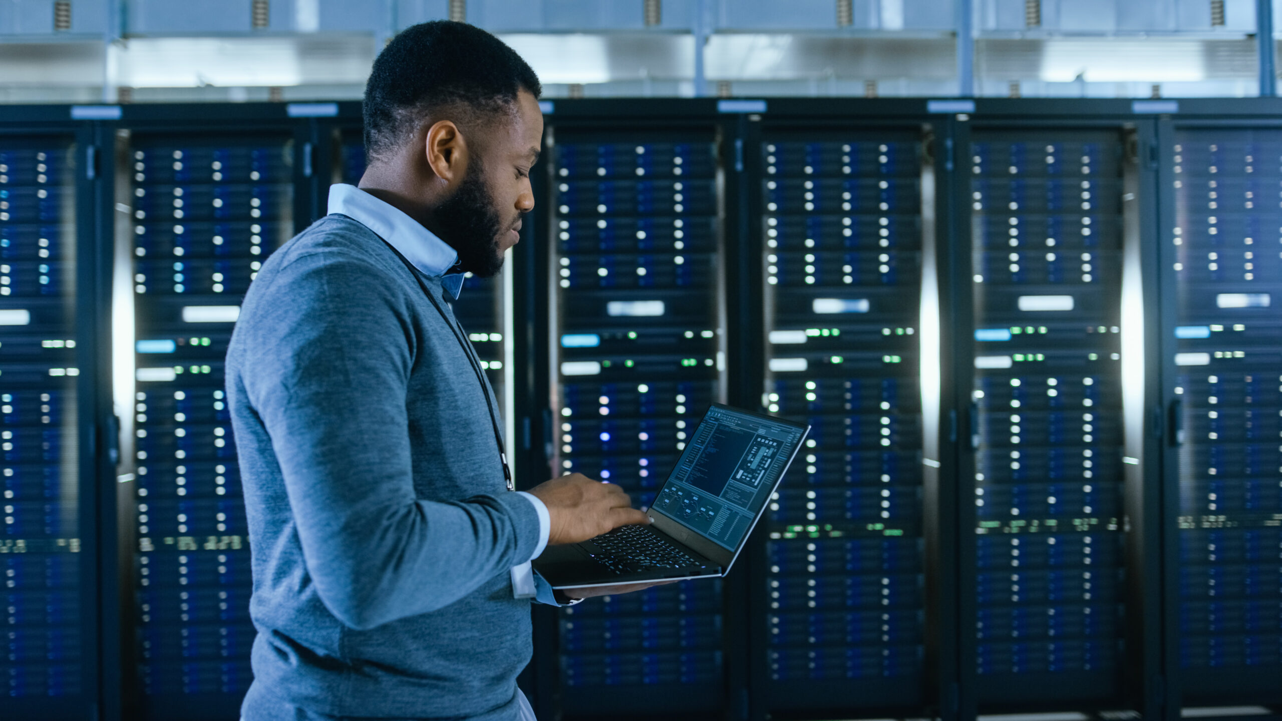 An IT professional conducting a security audit in a server room with a laptop.